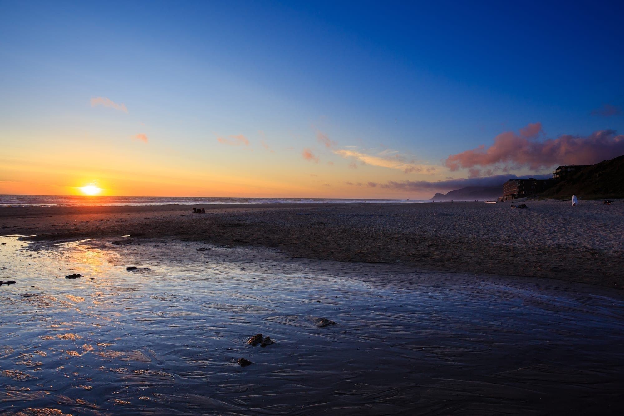 A serene beach at sunset with gentle waves and colorful sky reflections.