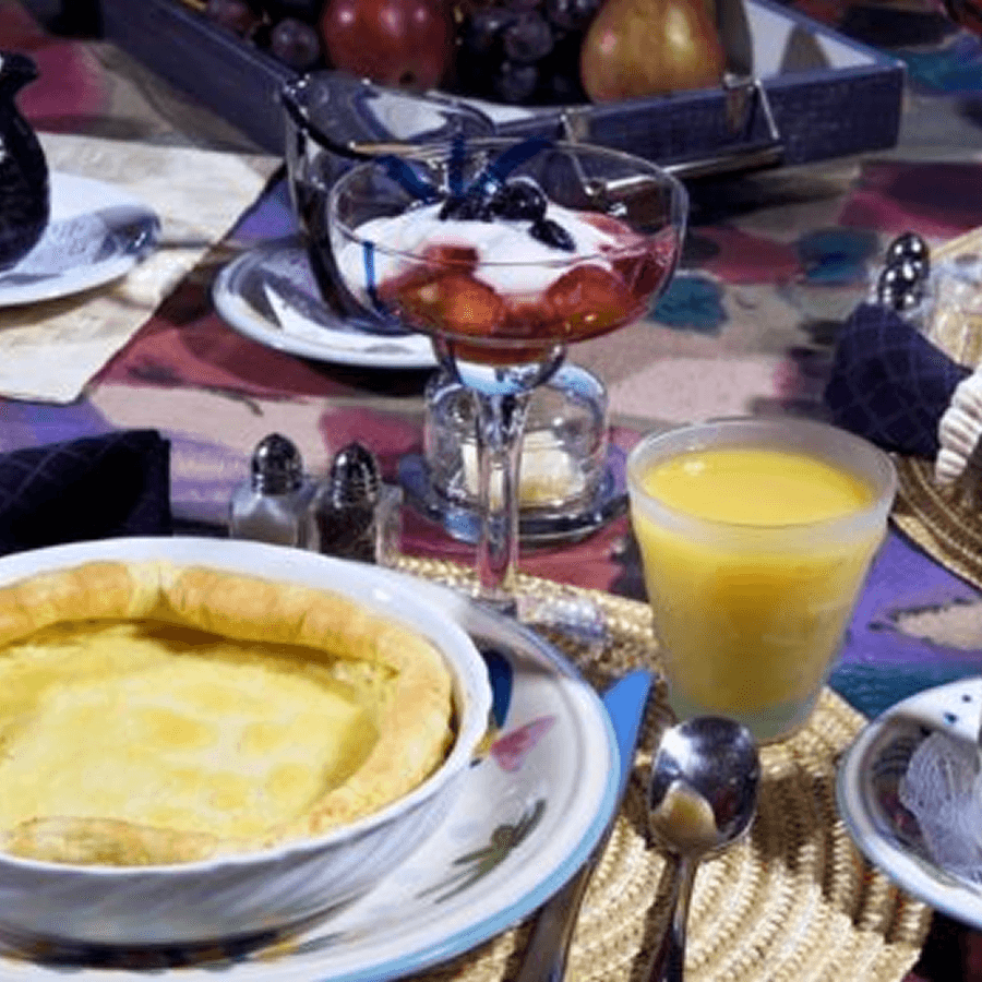 A table setting with a fruit salad in a glass, a bowl of creamy pie, and a glass of orange juice.