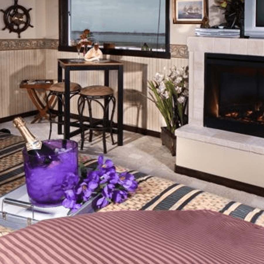 A cozy indoor setting featuring a fireplace, a small dining table with two stools, and decorative flowers.