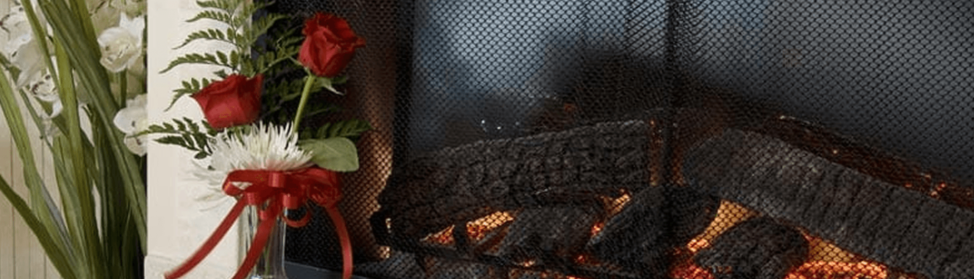 A cozy fireplace with burning logs beside a vase of red roses and white flowers.