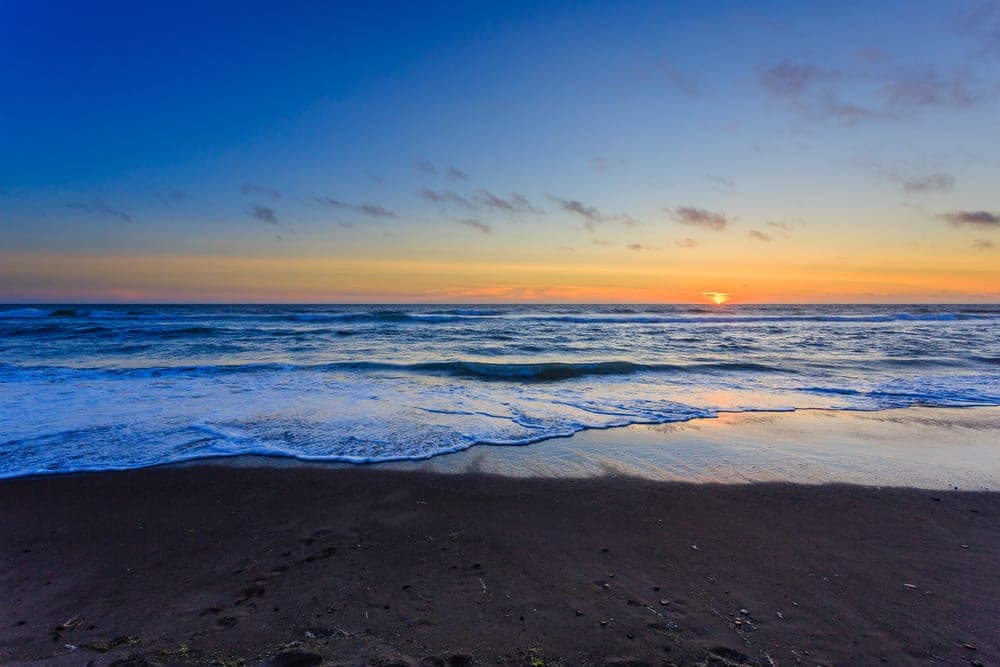 A serene beach at sunset, with gentle waves lapping at the shore under a colorful sky.